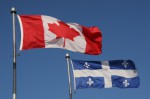 Quebec and Canadian flags blowing in front of a blue sky