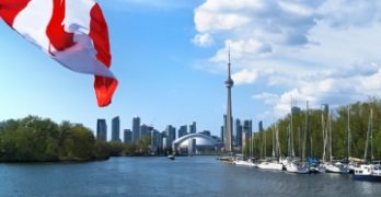 A Canadian flag flutters over a lake, with a view of Toronto in the background