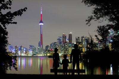 A family looks at the Toronto skyline at night, across Lake Ontario