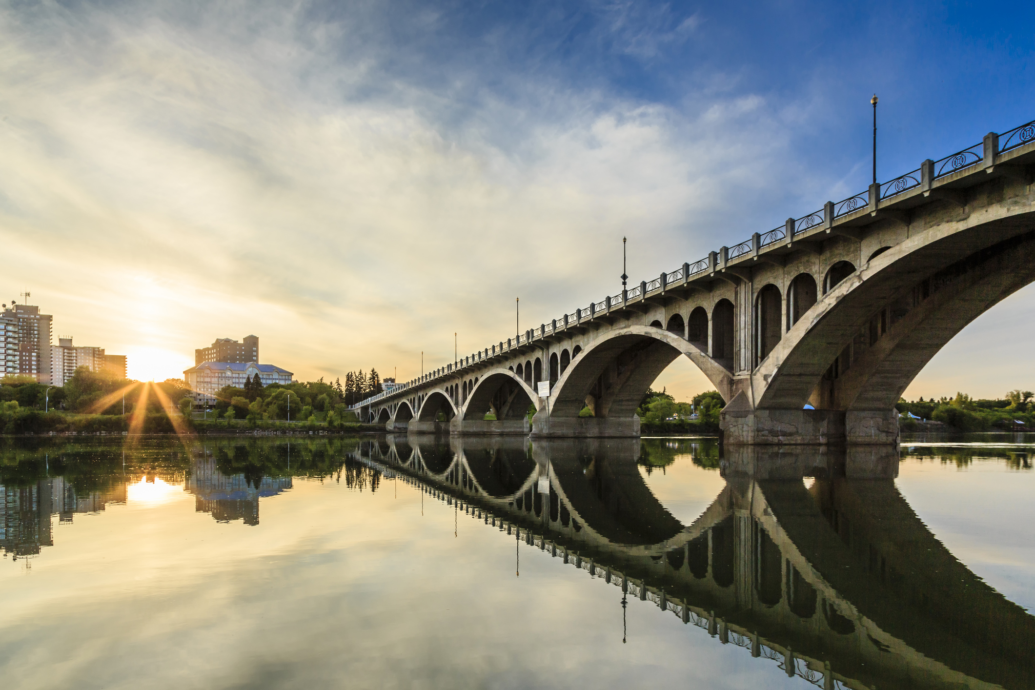 A warm summer sunset over the city of Saskatoon located in Central Canada where the calm waters of the South Saskatchewan River flows under the University Bridge.