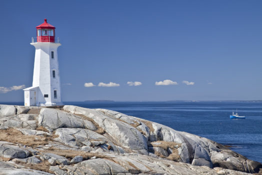 Peggy's Cove lighthouse, one of the major tourism destinations in Nova Scotia, Canada. Lobster boat gathering traps in the background.