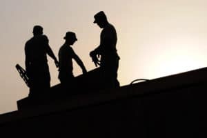 Three silouhettes of workers on a roof angled toward the sun