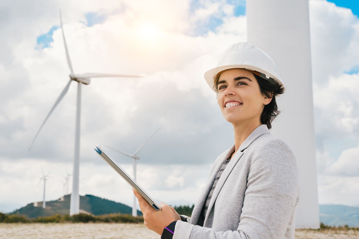 Environmental engineer stands in front of wind turbines holding tablet