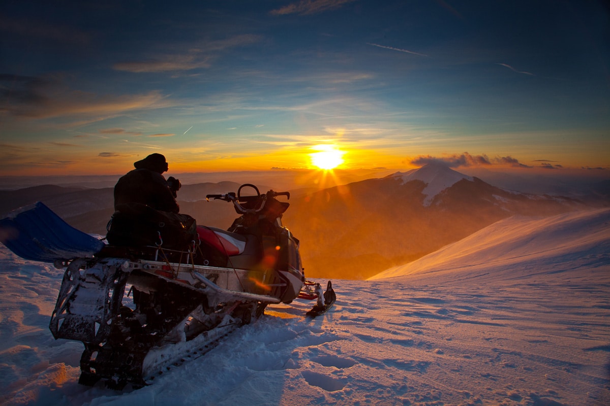 A person sitting on a snowmobile watching the sun set over Canadian mountains