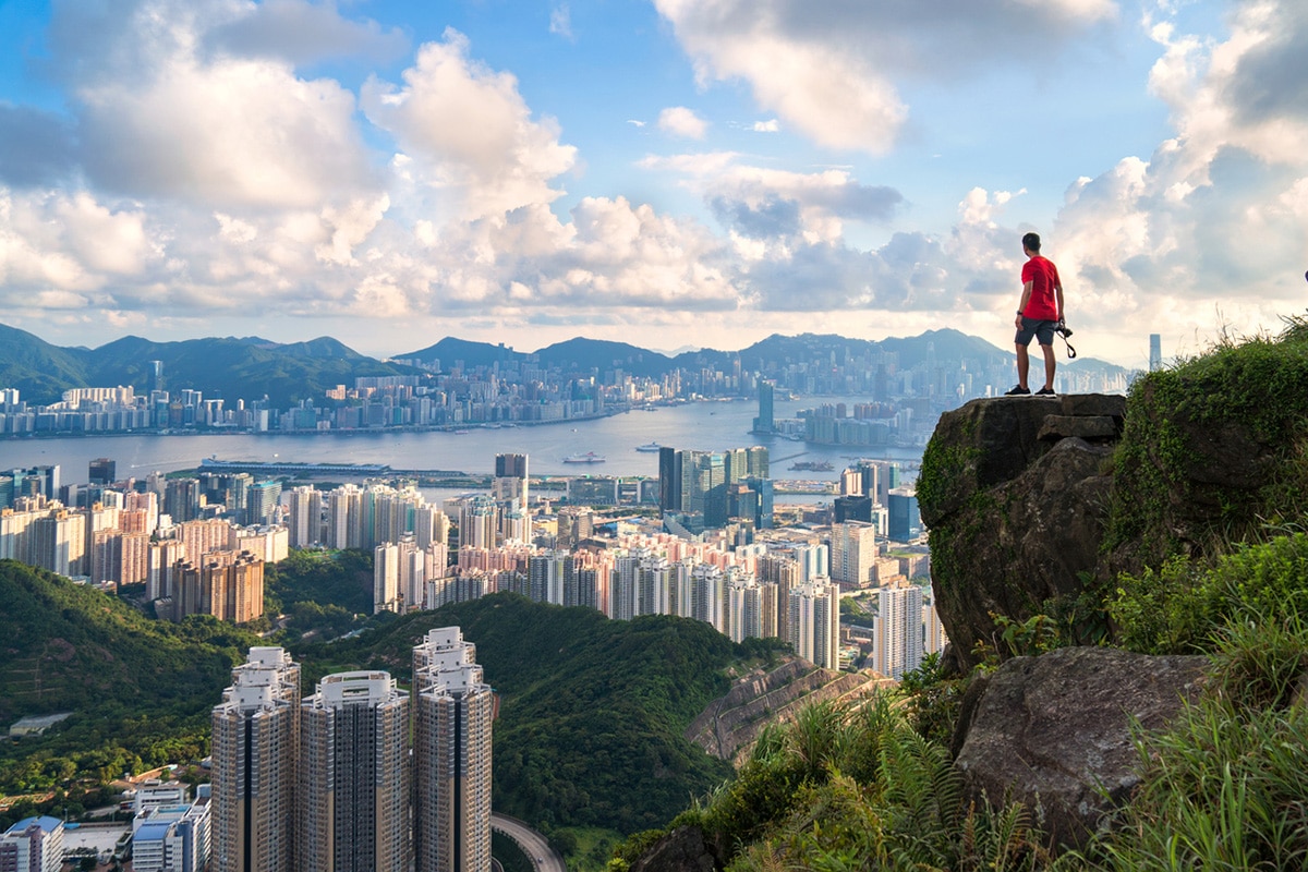 Photographer stands on rock overlooking Hong Kong skyline.