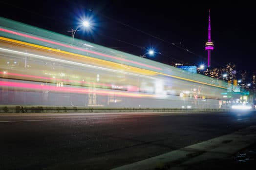 Bus speeding by on Toronto street, CN Tower glowing purple in the background