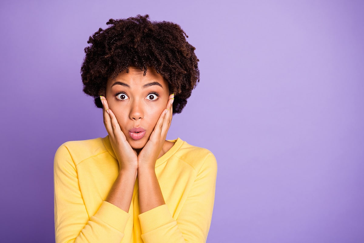 A woman holding her cheeks in her palms with a mortified expression on her face.