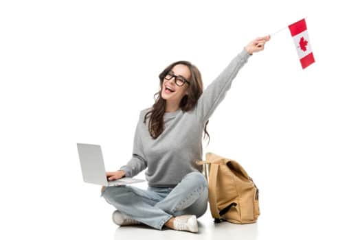 Excited woman waves Canadian flag, sitting cross-legged with laptop on her knee