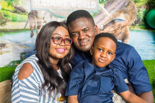 Ashiru family facing the camera, smiling. Kunle holds his son, Sultan, and his wife, Ibukun, in each arm.