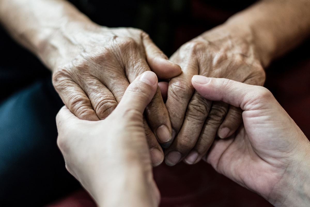 Young person's hands holding elderly person's hands