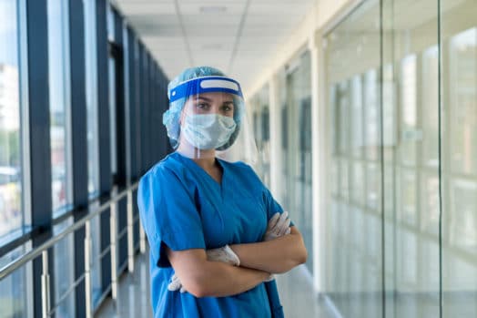 Nurse wearing COVID gear while standing in a long hallway