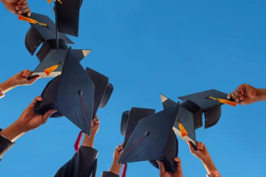 Graduates holding caps up to a blue sky