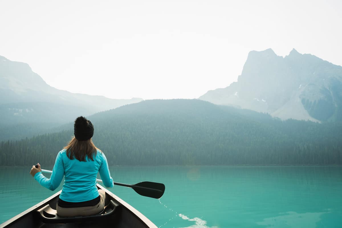 Woman canoeing on Canadian lake, looking at misty mountain