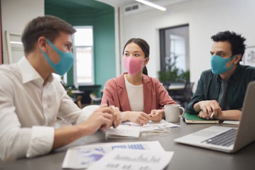 Three colleagues working at a desk, wearing masks during the pandemic