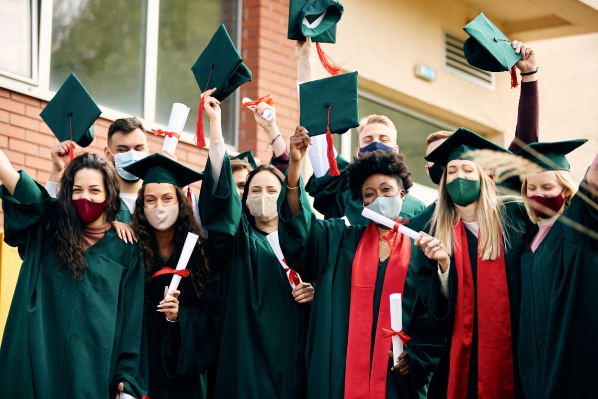 Graduates wearing surgical masks throw their caps.