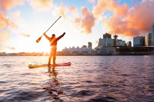 A person on a paddle board raises their arms on a winter morning in Vancouver.