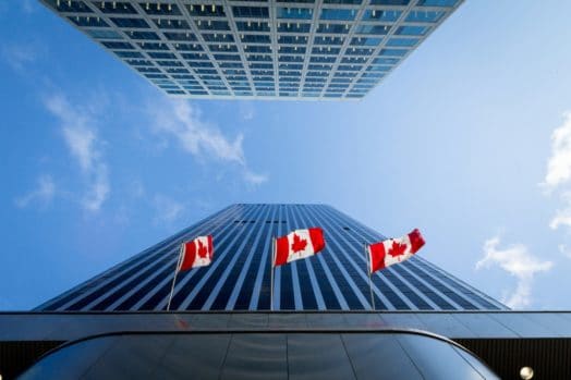 Tres banderas canadienses ondeando en el lateral de un edificio alto.
