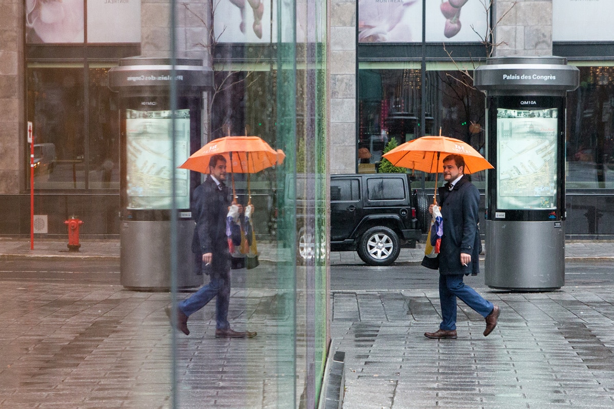 Man with orange umbrella walks by Palais de Congres in Montreal.
