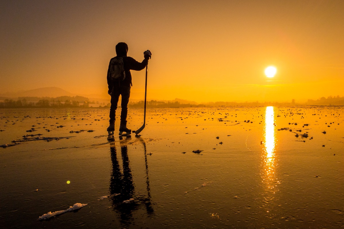 Silhouette of a hockey player on a lake watching the sunset