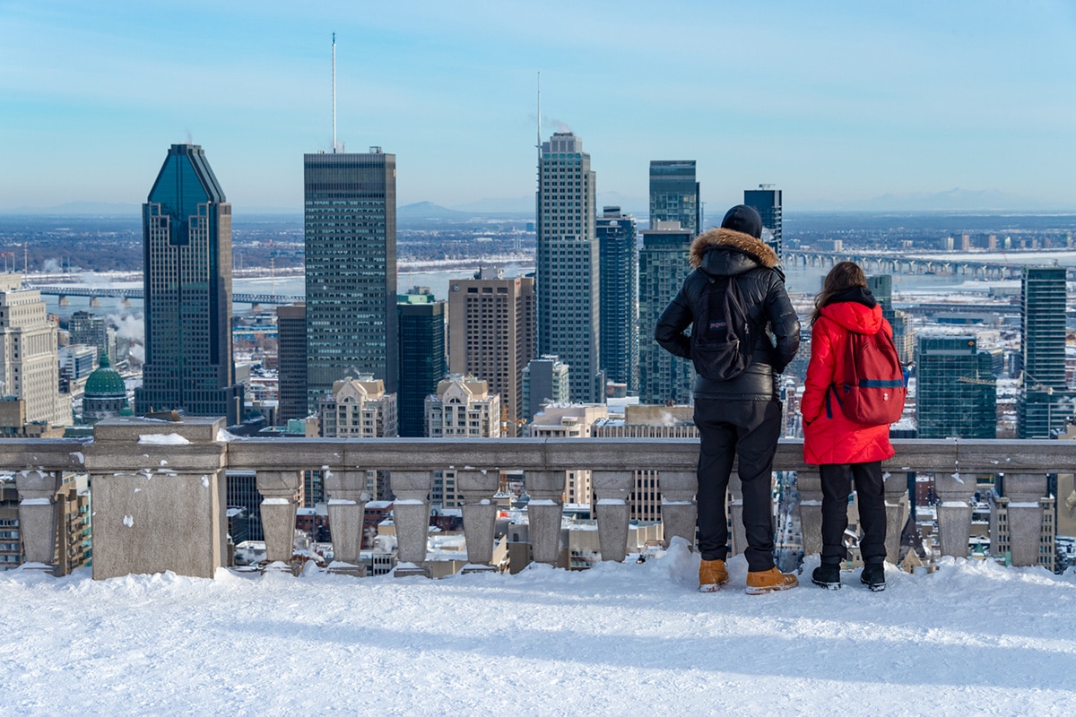 A couple gazes into the Montreal skylinne. Snow covers the ground.