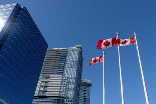 Three Canadian flags blowing in the wind near skyscrapers