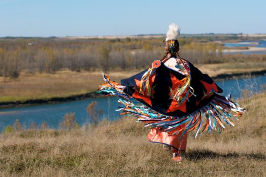 A woman performing a First Nations fancy shawl dance in a field alongside the river in Saskatoon, Saskatchewan.