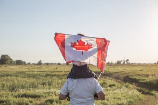 adulto con un niño sobre los hombros y un niño sosteniendo la bandera canadiense