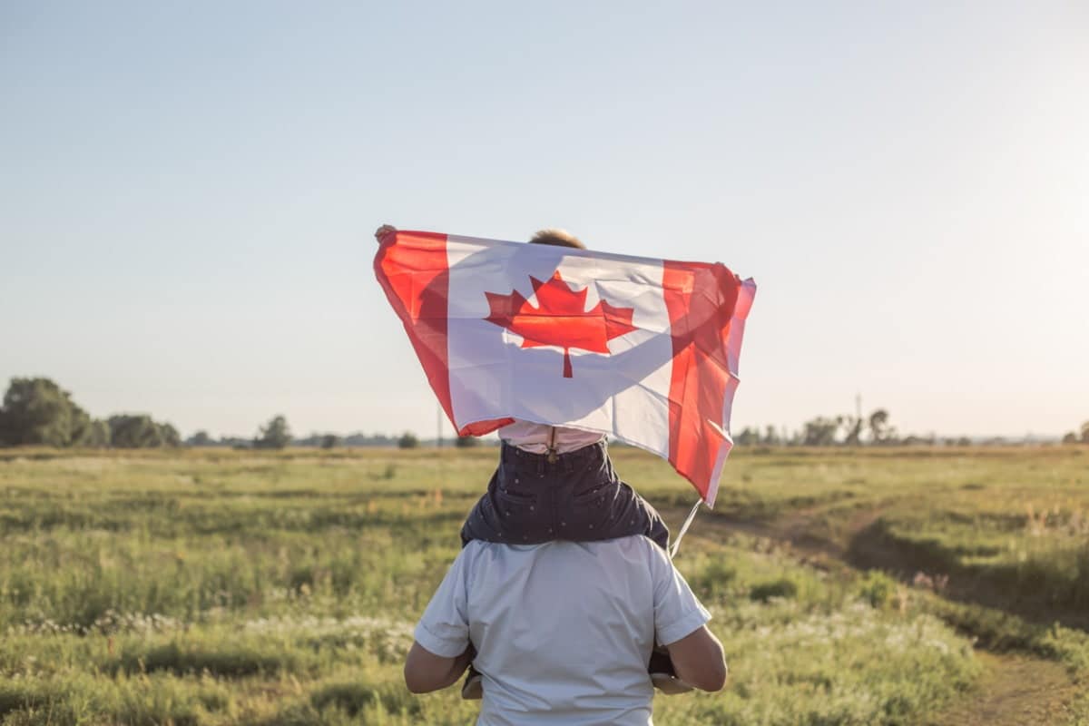 adult with child on shoulders and child holding Canadian flag