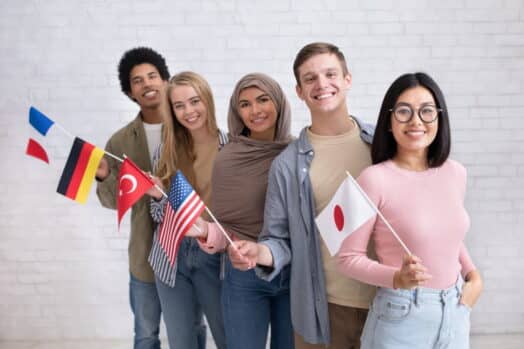 Grupo de estudiantes internacionales de pie y sonriendo juntos sosteniendo banderas de diferentes países - Japón, Estados Unidos, Turquía, Alemania