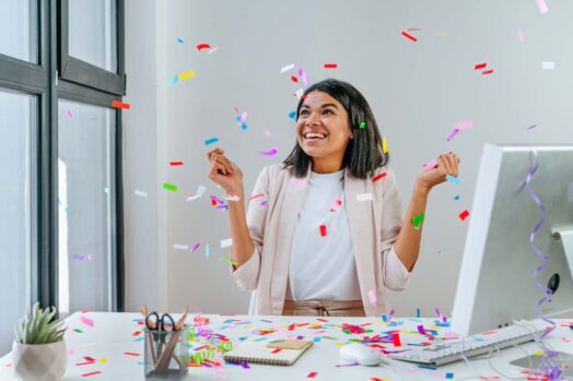 A lady at an office desk with confetti falling from the ceiling. Canada has recently announced that spouses of open work permit holders