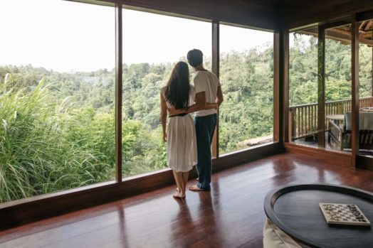 couple standing looking outside of a window towards a forest
