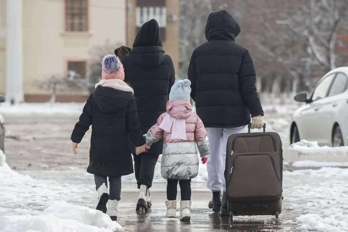 Family of four walking down snowy street with one suitcase