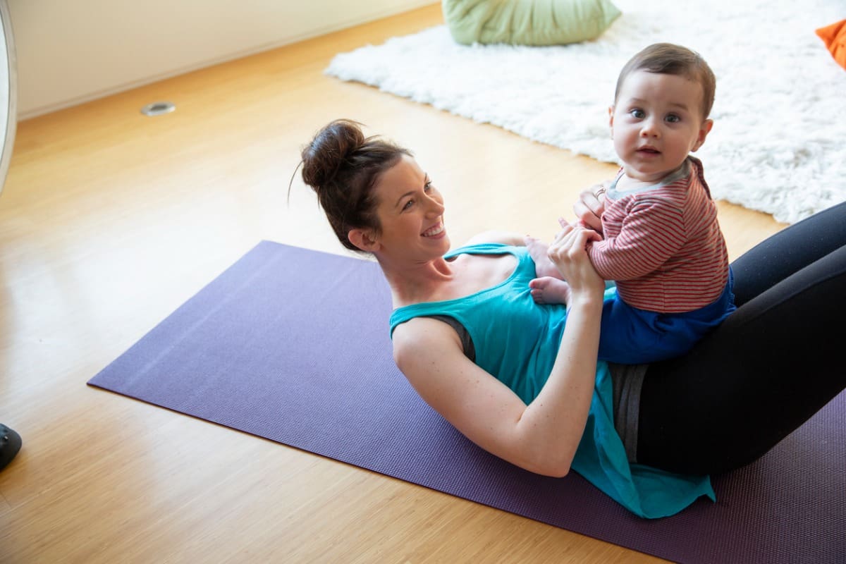 happy mother holding cute baby son on yoga mat at home