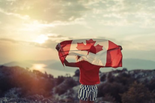 Una chica sentada en una montaña con vistas al bosque.  Se espera que la inmigración ayude en gran medida a Canadá a recuperarse y fortalecer su economía.
