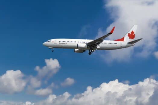 Avión comercial con bandera de Canadá en la cola y fuselaje aterrizando o despegando del aeropuerto con cielo azul nublado en el fondo