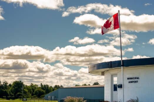 Edificio del aeropuerto municipal y hangares con una bandera de Canadá contra un cielo azul nublado de verano