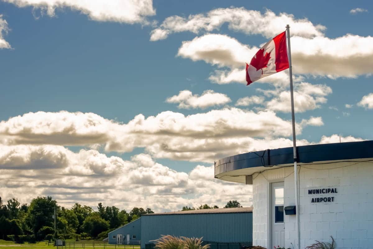 Municipal airport building and hangars with a Canada flag against a blue cloudy summer sky