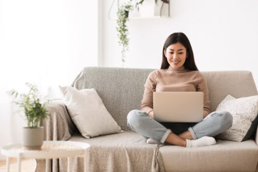 girl sitting on her couch with legs crossed browsing on her computer/laptop