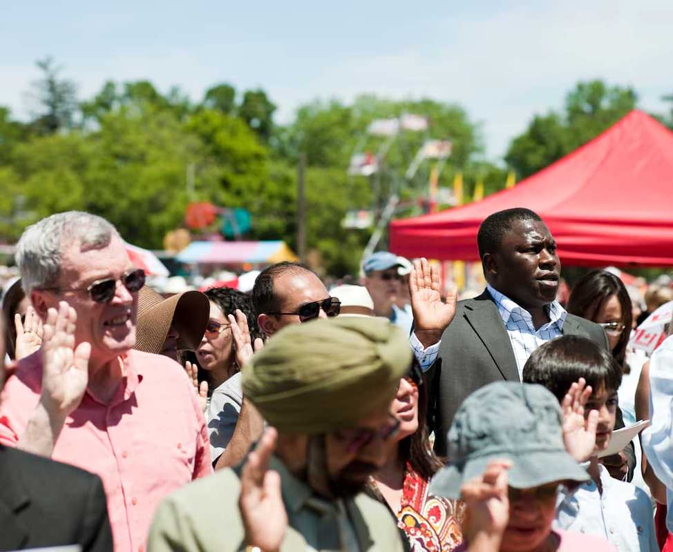 A multi-ethnic group of people swearing the oath during their Canadian citizenship ceremony