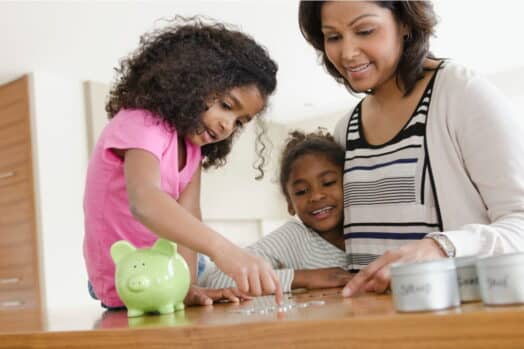 Mamá enseñando a sus hijas sobre el dinero contando monedas y usando una alcancía