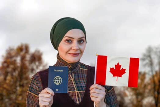 Mujer musulmana sonriendo a la cámara con pasaporte y bandera canadiense