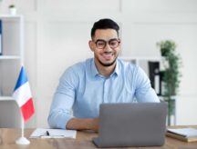 A man sitting at a desk with a small French flag and laptop.