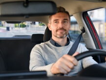 Happy man driving car looking into rearview mirror