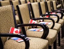 A row of chairs at a citizenship ceremony, with Canadian flags and pamphlets on each chair.