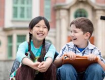 Two children smiling in front of a school building. Canadians spend a varying amount on child expenses, depending on family composition and province of residence. Read on to learn more