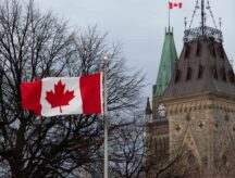 The Canadian Flag flies in full in front of the Parliament of Canada, the Peace Tower is seen in the background on a cloudy day in Ottawa.