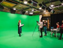 A group of people working on a film set, with a large green screen in the background
