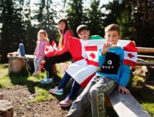 Family of mother with three kids hold large Canadian flag celebration in mountains.