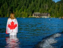 Summer scene of the Cultus Lake with a patriot woman in the foreground holding up a Canadian flag. Chilliwack, British Columbia, Canada