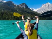 Two woman on Lake Louise hold their oars to the sky. While Canada doesn't allow sponsorship of siblings for PR, Canadians do have options to support their sibling's move to Canada.